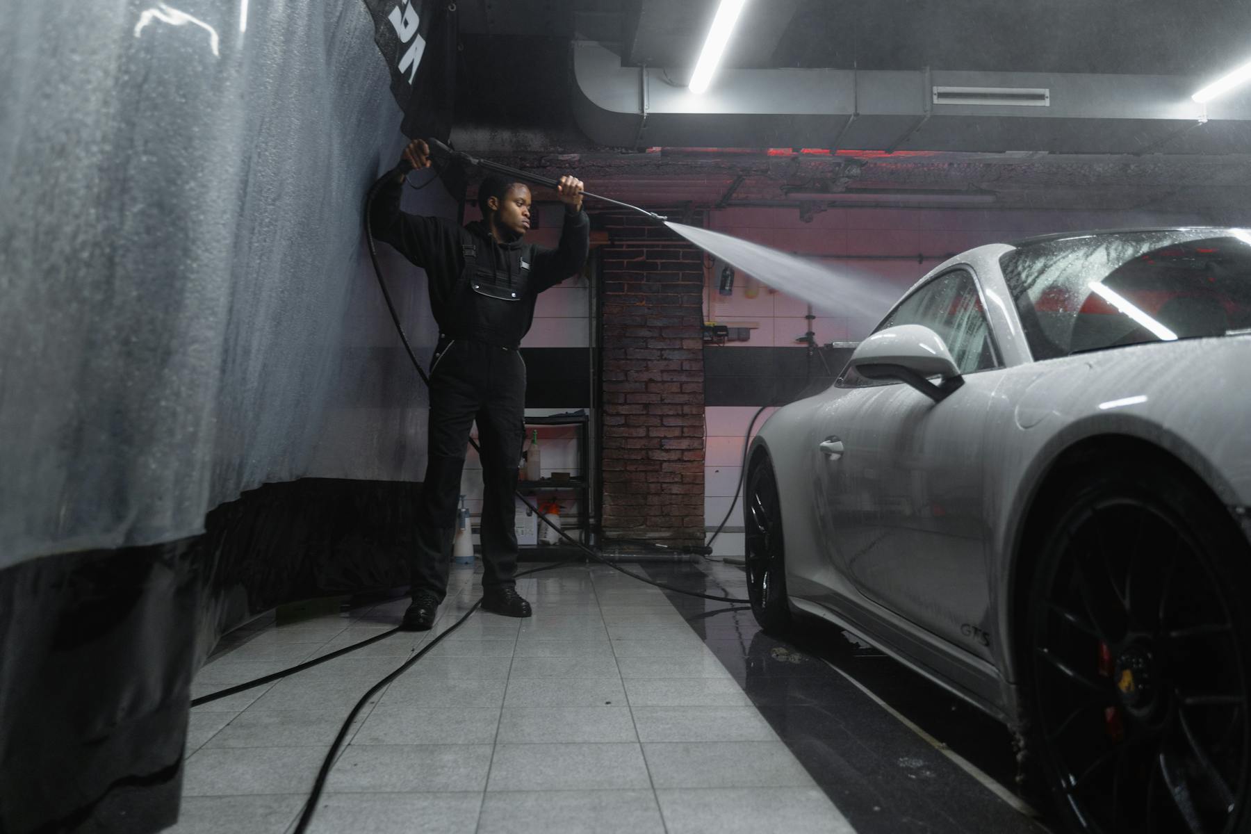 Detailer pressure washing a white sports car